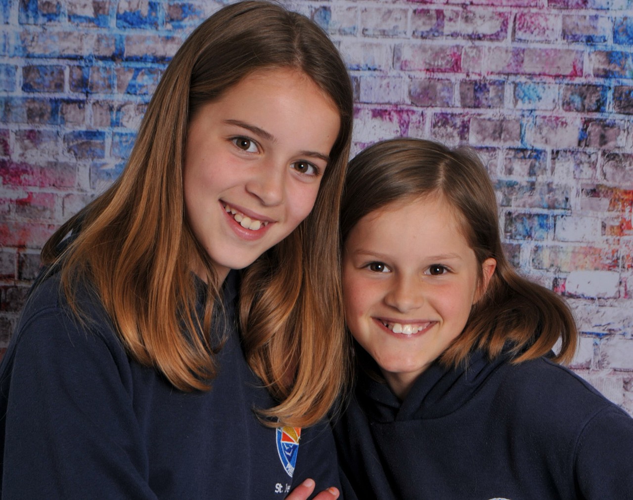Two friends smiling in front of a colourful painted brick backdrop